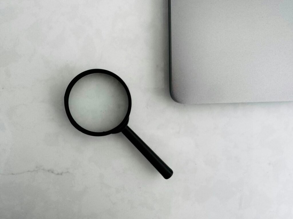 Magnifying glass beside a laptop, representing troubleshooting why a website is not showing up on Google search results